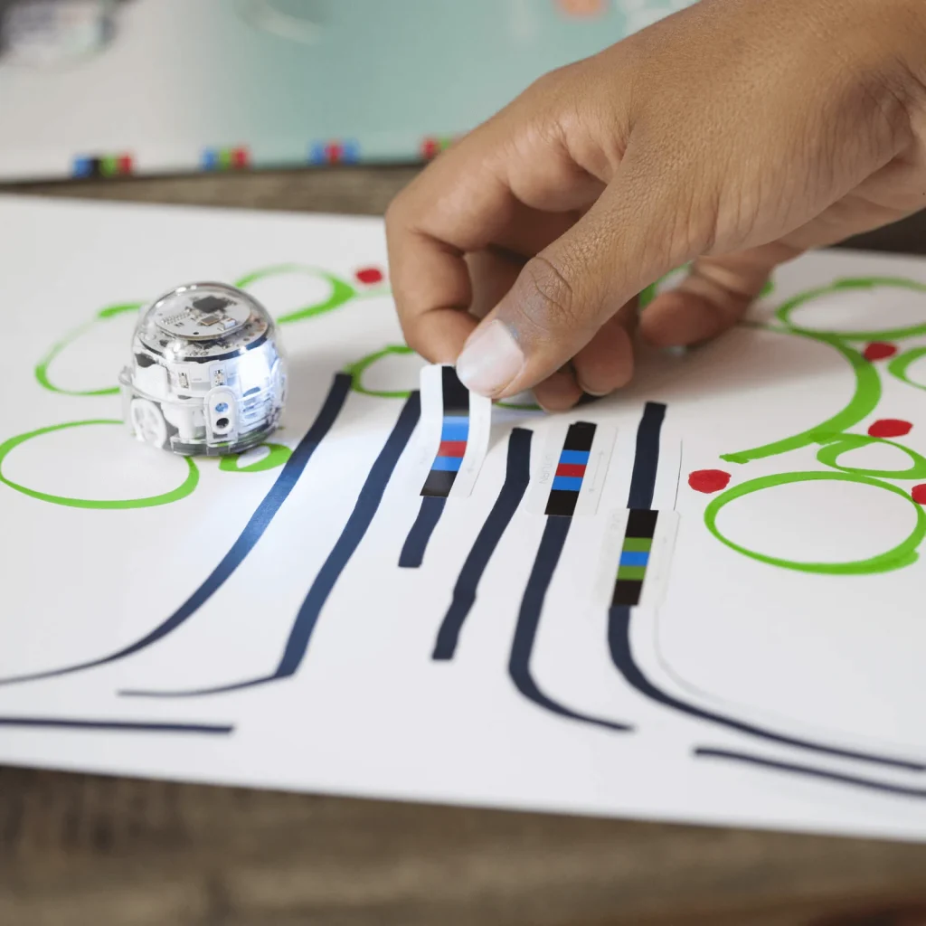 Een hand plaatst kleurcodestickers op een route naast Ozobot Evo